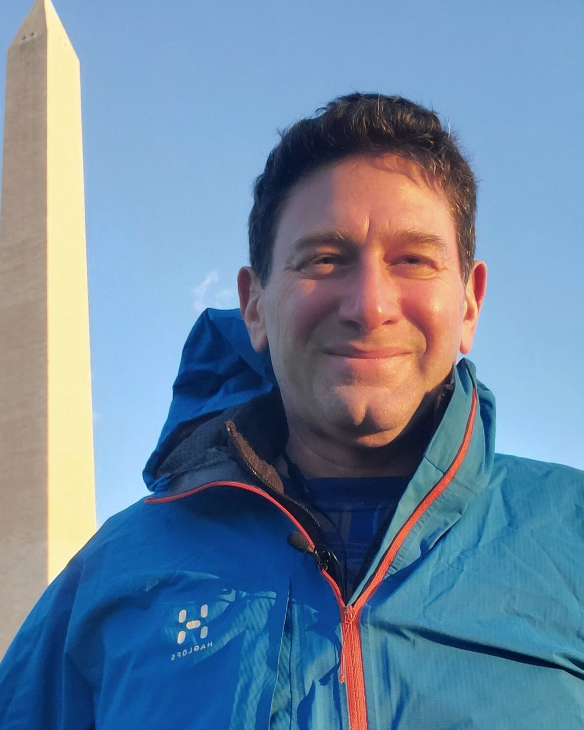 Brian Germain outdoors in a blue jacket, smiling, the Washington Monument behind him