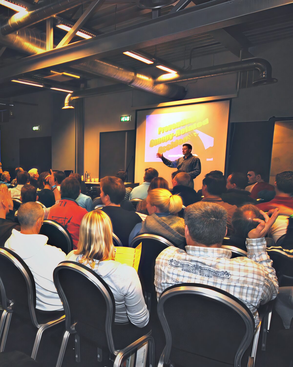 A full conference hall seen from the back rows, Brian Germain presenting at the screen